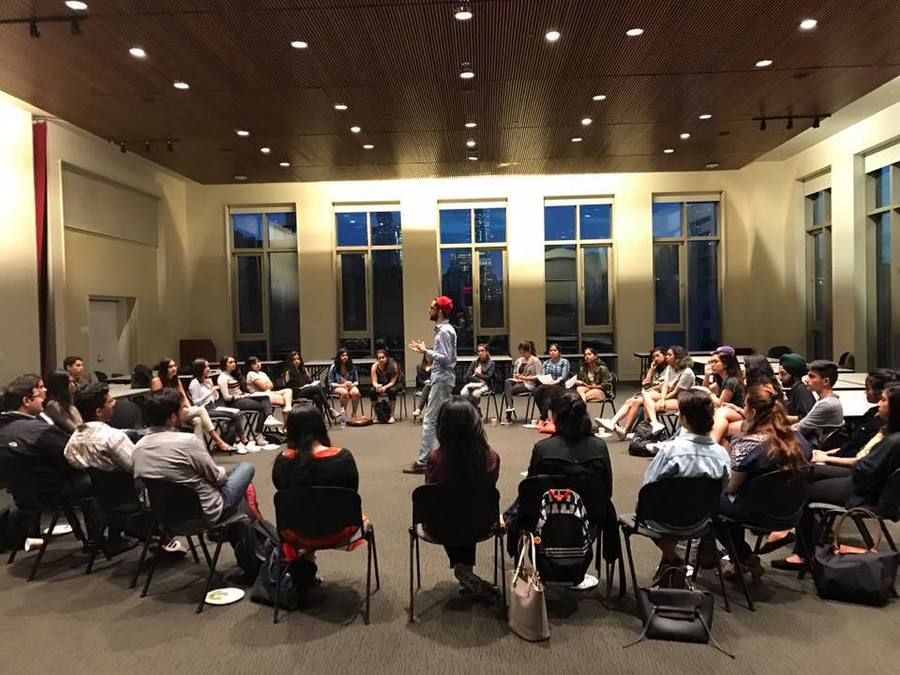Dozens of students seated in a wide circle, one standing to speak