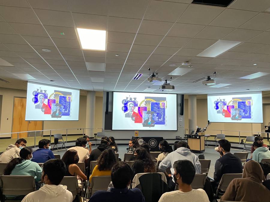 A lecture theatre full of students watching three projected screens