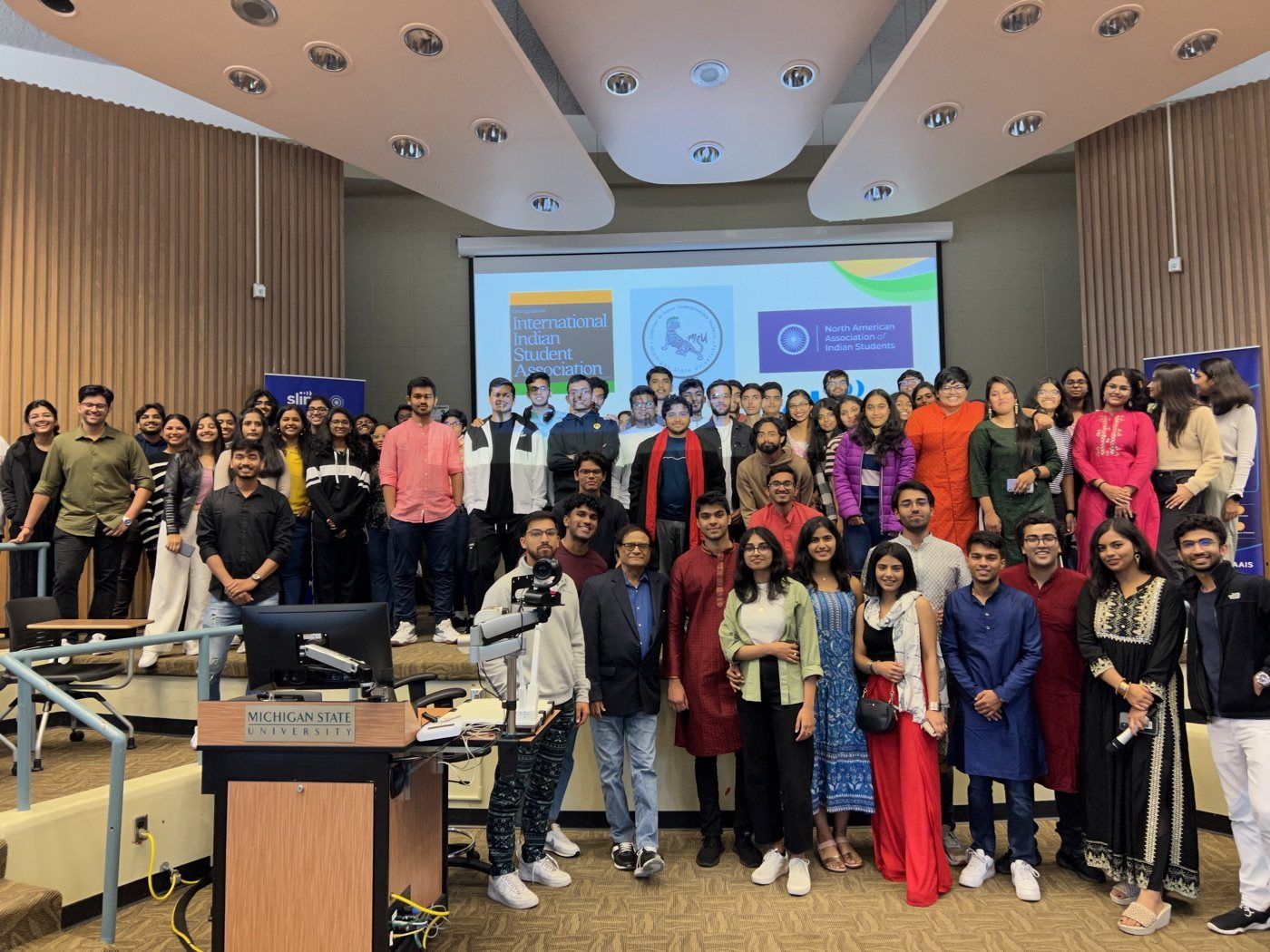 A large group photo of NAAIS students in front of a projector screen